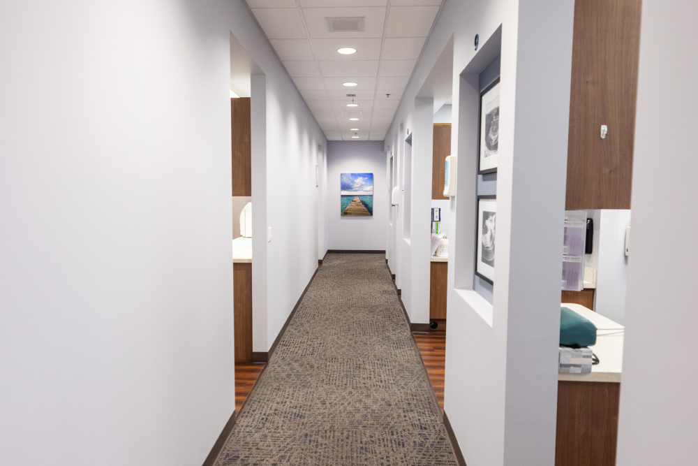 img slider photo Modern dental office hallway with white walls, wood accents, and recessed lighting leading to treatment areas.